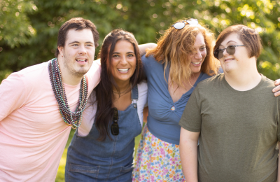 A group of young adults stand arm-in-arm with trees in the background.